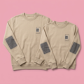 Pair of matching beige crewneck sweatshirts on soft pink background