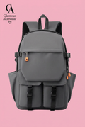 Grey backpack with two lower buckle pockets and orange zip accents on soft pink background