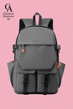 Grey backpack with two lower buckle pockets and orange zip accents on soft pink background