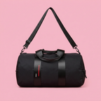 Black barrel duffle bag with wide straps on soft pink background