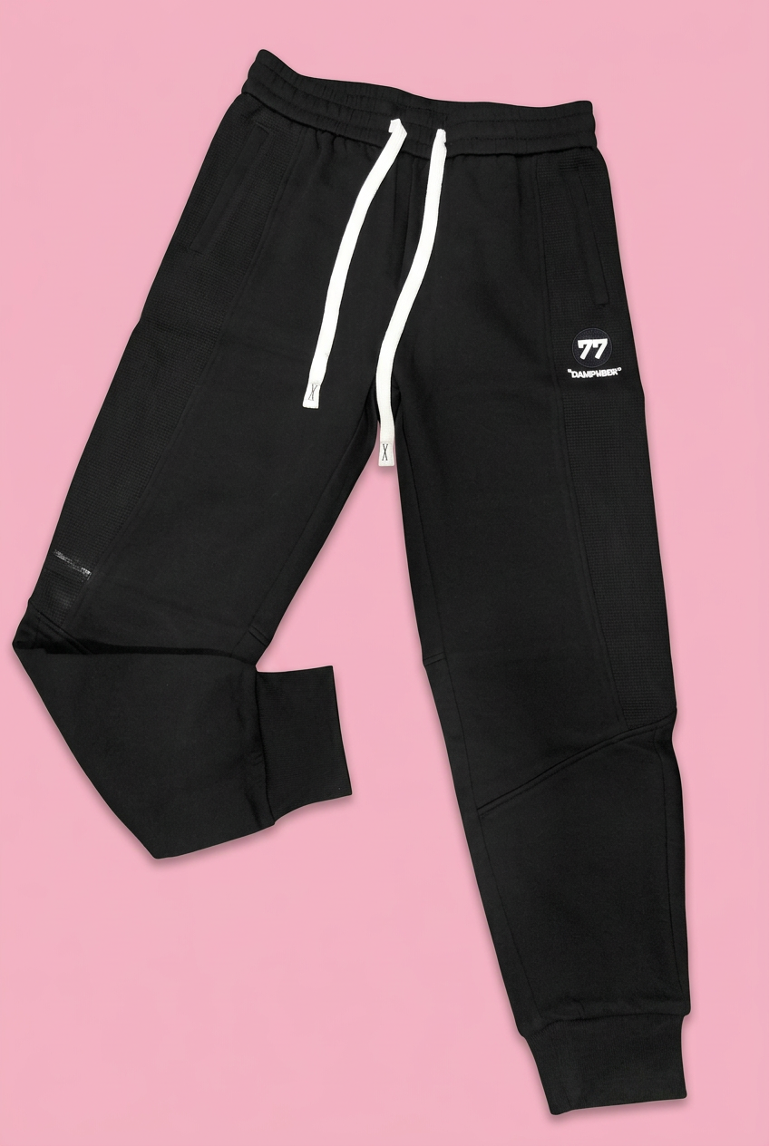 Black drawstring joggers with white 77 emblem on soft pink background