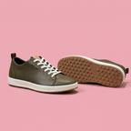Olive lace-up sneakers with white midsole and tan outsole on soft pink background