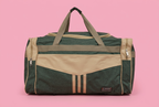 Dark green and beige travel duffel bag on soft pink background