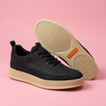 Black lace-up sneakers with cream soles on soft pink background
